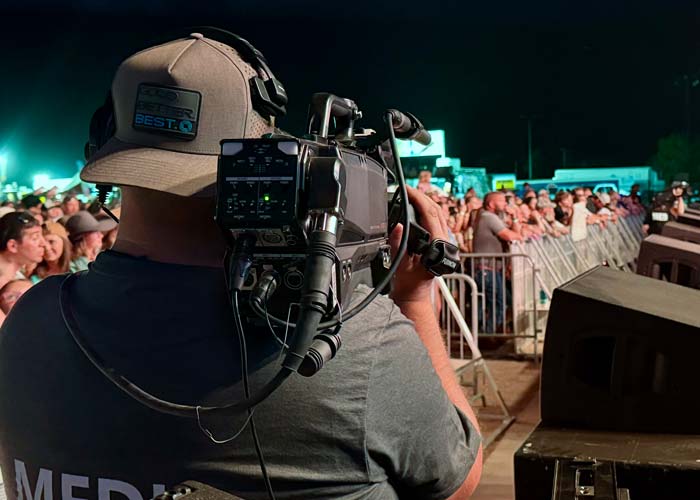 Camera operator running handheld shoulder hitachi camera at field level with SMPTE fiber at live sporting event or concert