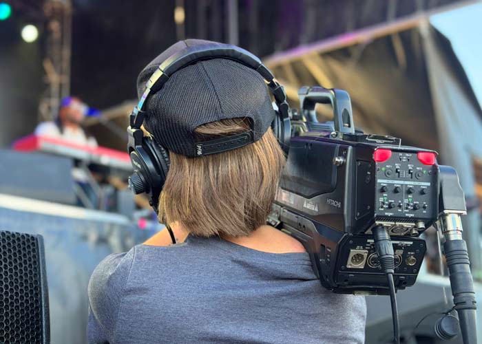 Camera operator running handheld shoulder hitachi camera at field level with SMPTE fiber at live sporting event or concert